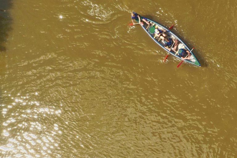 Eine Gruppe sitzt in einem Boot auf braunem Wasser, umgeben von Sonnenlicht.