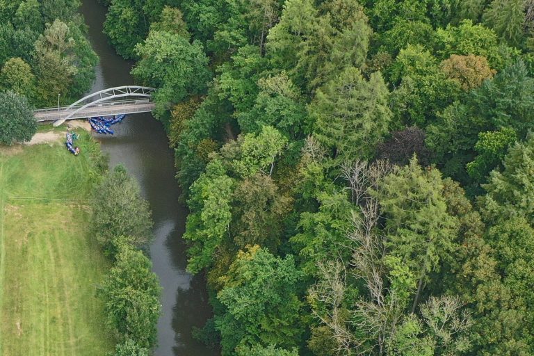 Brücke über einen schmalen Fluss, umgeben von dichten grünen Bäumen.