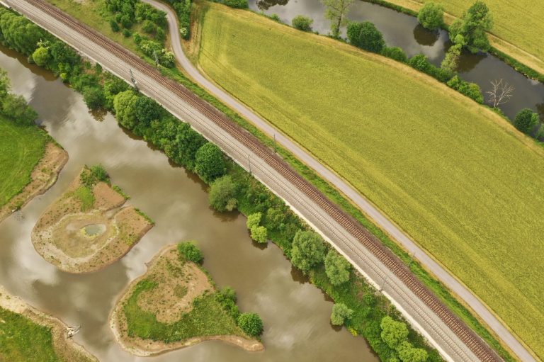 Luftaufnahme einer kurvigen Straße neben einem Fluss und Feldern.
